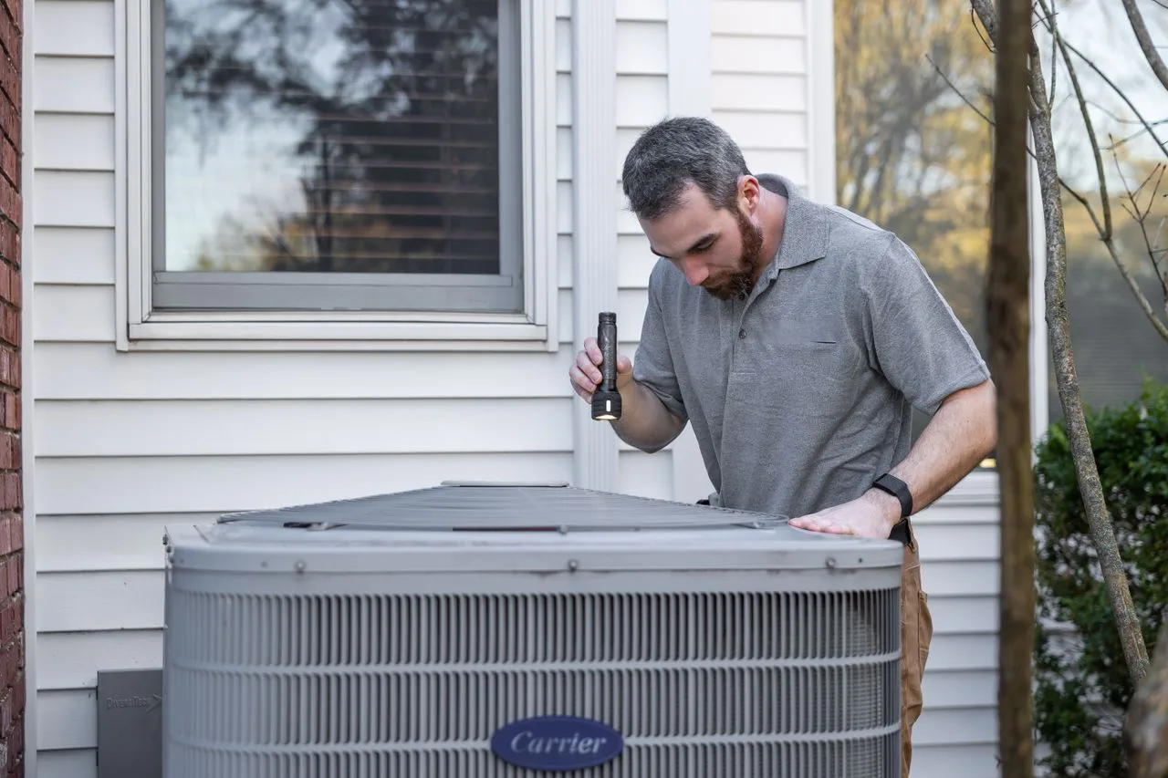 Maintenance technician inspecting an outdoor HVAC unit with a flashlight