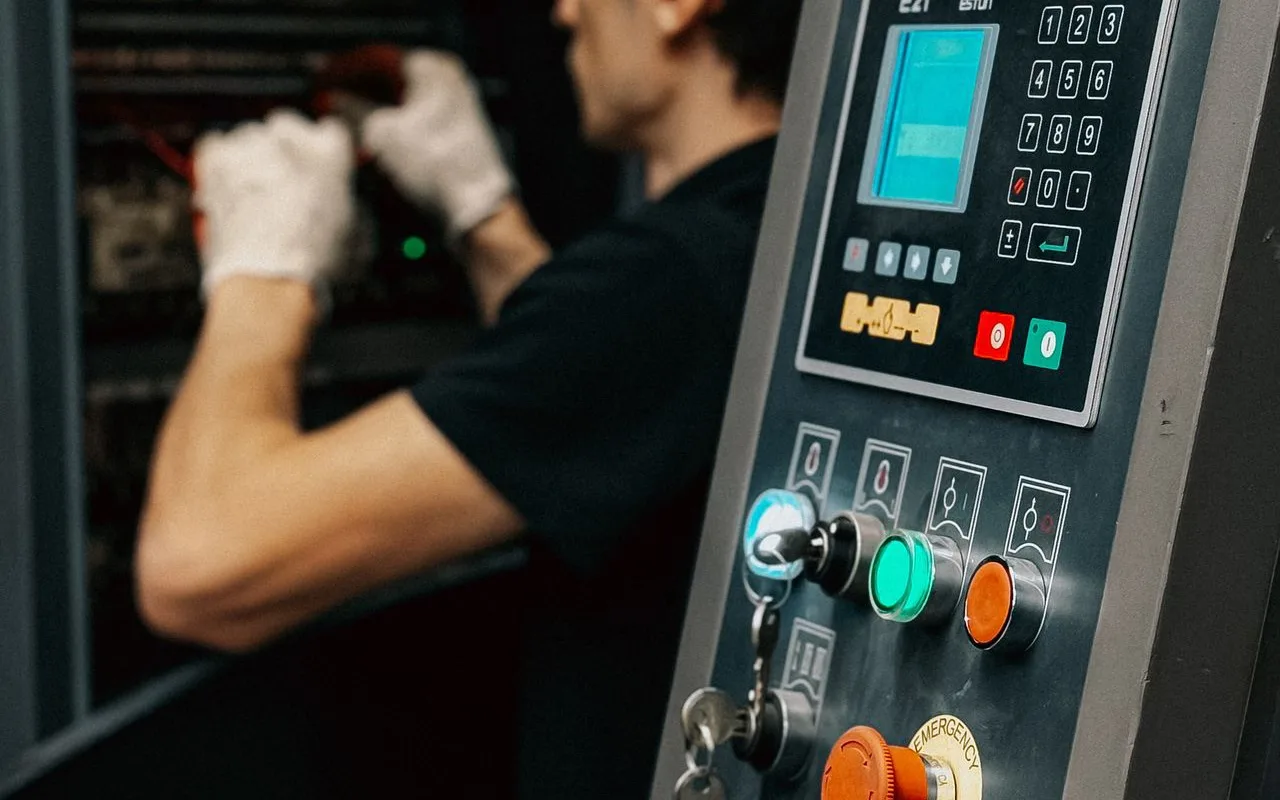 Maintenance technician in gloves servicing industrial equipment at a control panel