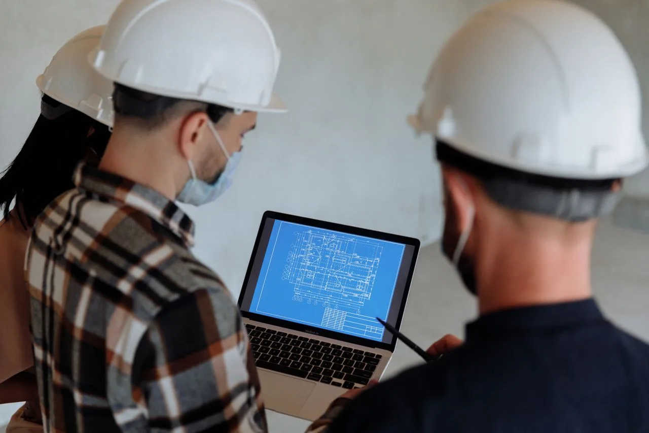 Construction team in hard hats reviewing a building plan on a laptop on site